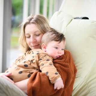 Mum cuddling baby who looks slightly uncomfortable