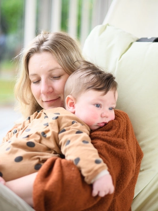Mum cuddling baby who looks slightly uncomfortable