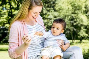 Eine Frau hält ein Baby im Freien, das sie mit einem Löffel füttert.