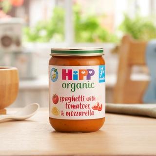 HiPP Organic Spaghetti with tomatoes & mozzarella on a dining table next to a bowl and spoon