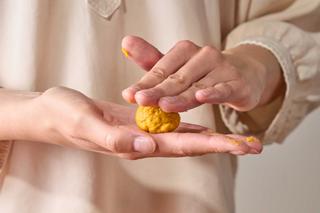 Hände formen eine kleine Kugel aus gelbem Teig oder Material