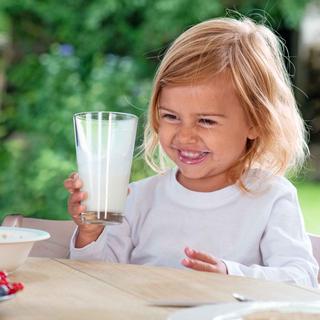 Ein fröhliches Kind hält ein Glas mit weißer Flüssigkeit, vermutlich Milch, in der Hand.