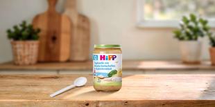 HiPP Bio Babyglas Tagliatelle mit Alaska-Seelachsfilet in Rahmbrokkoli ab dem 10. Monat auf Holztisch mit Löffel in heller Küche