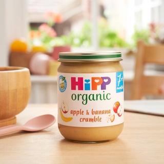 HiPP Organic Apple & Banana Crumble Jar on a dining table next to a bowl and spoon