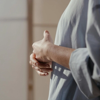 An image of a woman from shoulder to waist side on, holding her hands