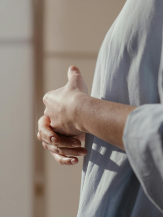 An image of a woman from shoulder to waist side on, holding her hands