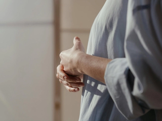 An image of a woman from shoulder to waist side on, holding her hands