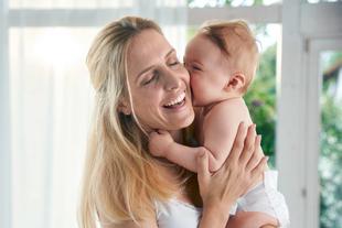 Ein zärtlicher Moment zwischen einer Mutter und ihrem Baby, in dem die Mutter ihr Baby freudig an ihr Gesicht drückt.