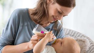 Eine Frau füttert ein Baby mit der Flasche, beide sitzen bequem.