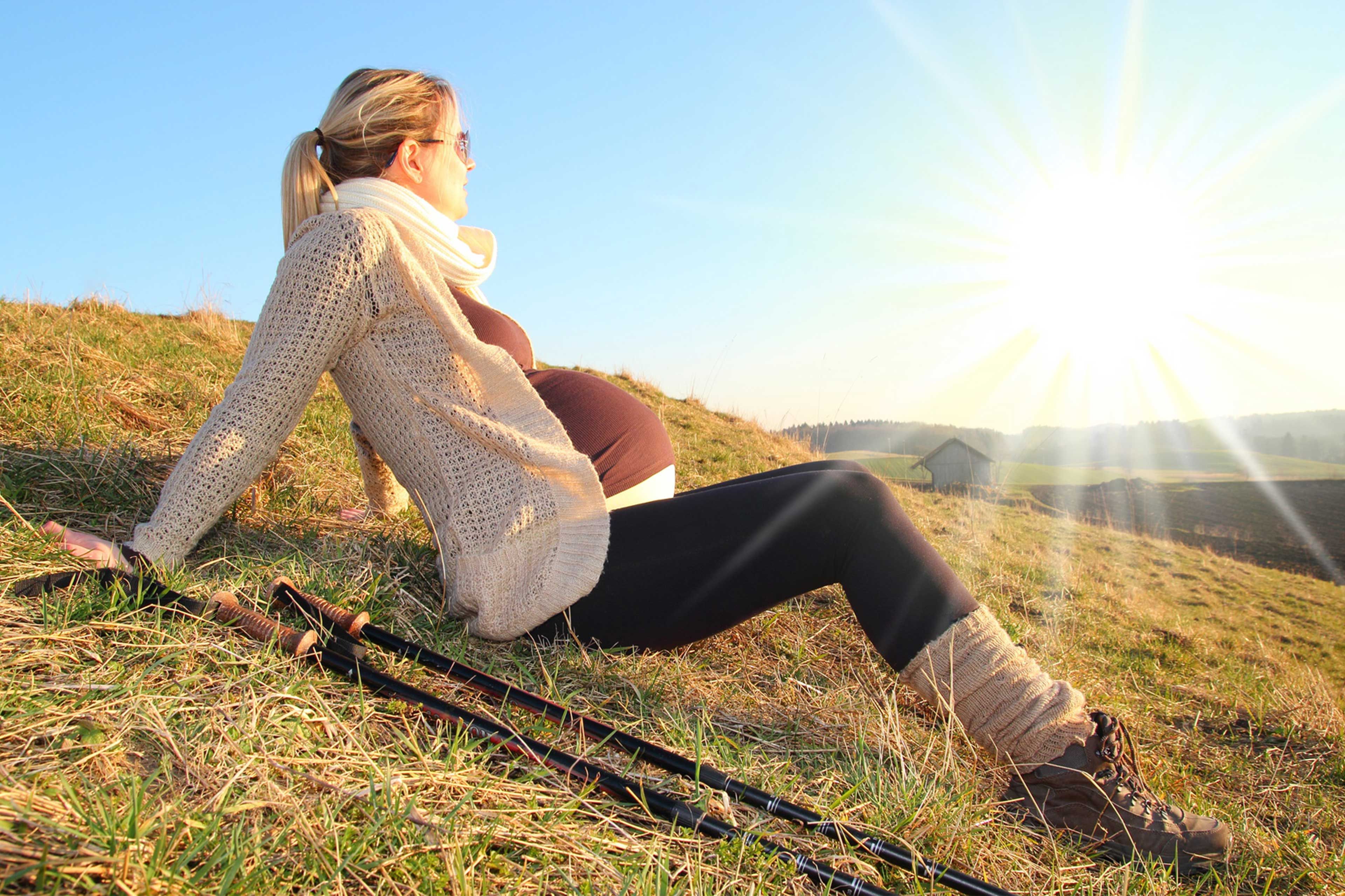 Eine Frau sitzt auf einem grasbewachsenen Hügel und blickt bei strahlend blauem Himmel und strahlendem Sonnenschein auf den Horizont.