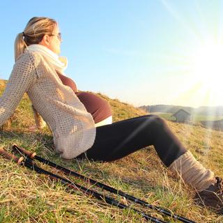 Eine Frau sitzt auf einem grasbewachsenen Hügel und blickt bei strahlend blauem Himmel und strahlendem Sonnenschein auf den Horizont.