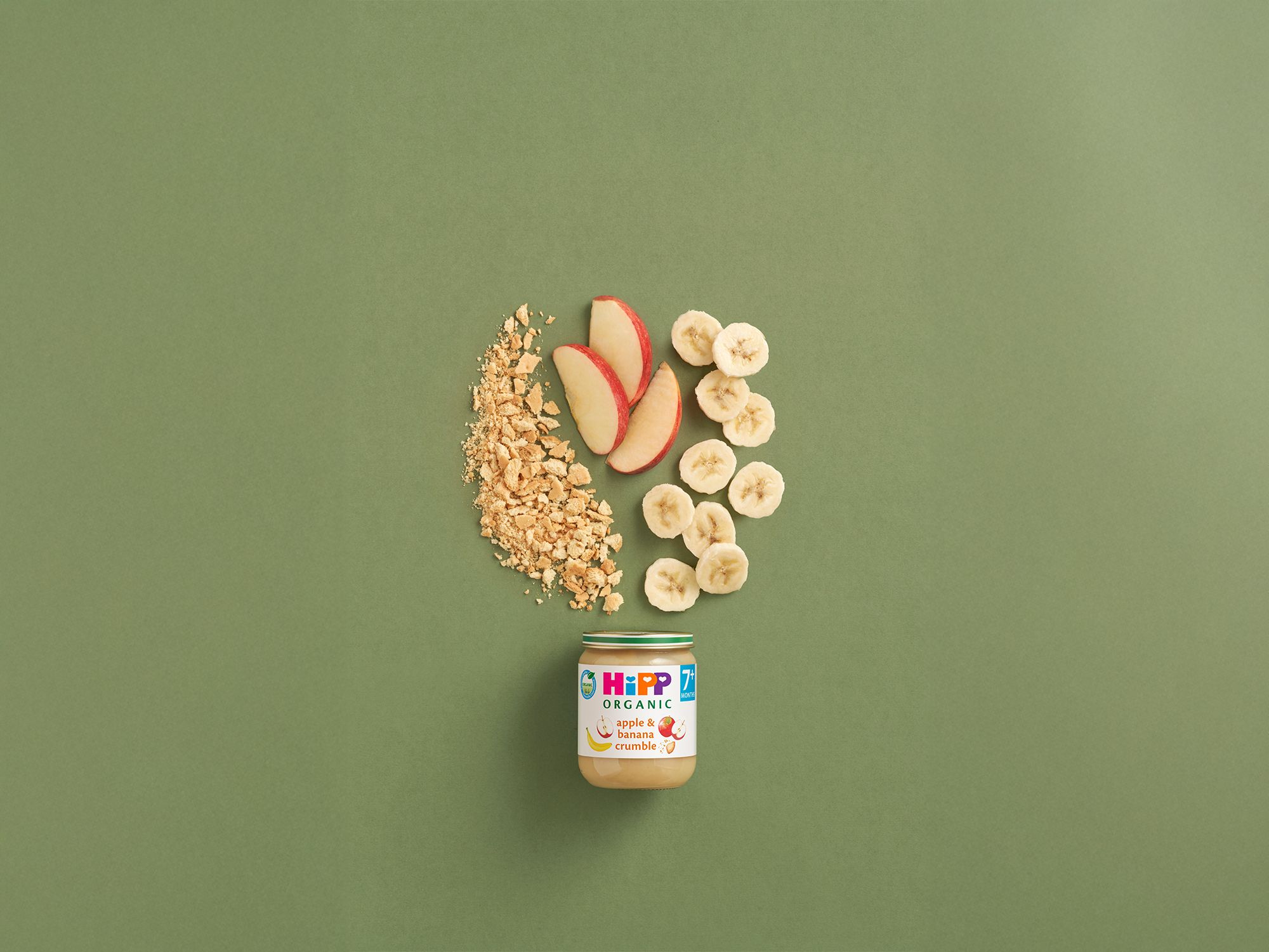 HiPP Organic Apple & Banana Crumble jar with apple and banana slices and biscuit crumble on a green background