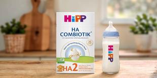 HiPP HA COMBIOTIK® HA 2 Packung und gefülltes Babyfläschchen auf einem Holztisch in einer warmen Küchenumgebung