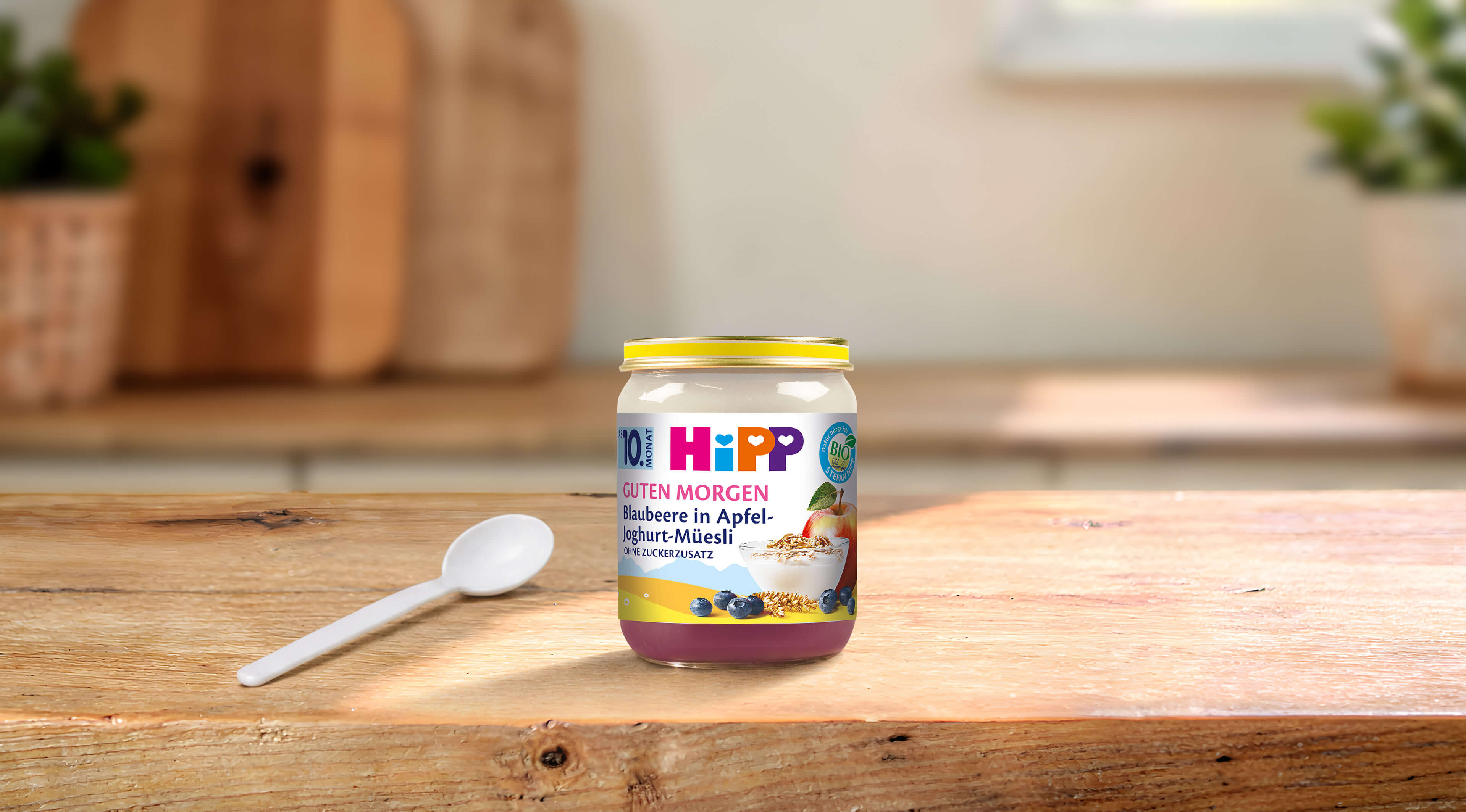 HiPP Guten Morgen Blaubeere in Apfel-Joghurt-Müesli Bio-Babygläschen auf Holztisch mit Löffel in heller Küche