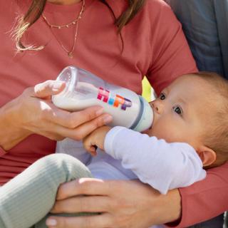 Baby liegt entspannt im Arm und trinkt Milch aus einer HiPP-Flasche, liebevoll gehalten von einem Elternteil