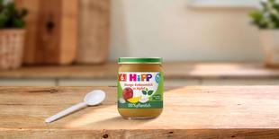 HiPP Bio Babygläschen Mango Kokosmilch in Apfel, 100 % pflanzlich, auf Holztisch mit Löffel in heller Küchenumgebung
