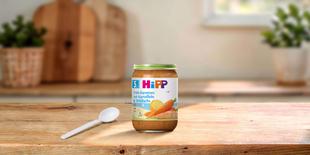HiPP Früh-Karotten mit Kartoffeln & Wildlachs Bio-Babygläschen auf Holztisch mit Löffel in heller Küche