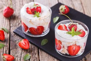 Zwei Gläser, gefüllt mit einem cremigen Dessert, garniert mit frischen Erdbeeren und Minzblättern.