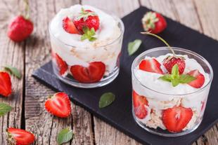 Zwei Gläser, gefüllt mit einem cremigen Dessert, garniert mit frischen Erdbeeren und Minzblättern.