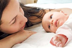 Ein zärtlicher Moment zwischen einer Mutter und ihrem Baby, in dem die Mutter ihr Gesicht sanft neben das des Babys legt und beide einen heiteren und intimen Moment zu teilen scheinen.