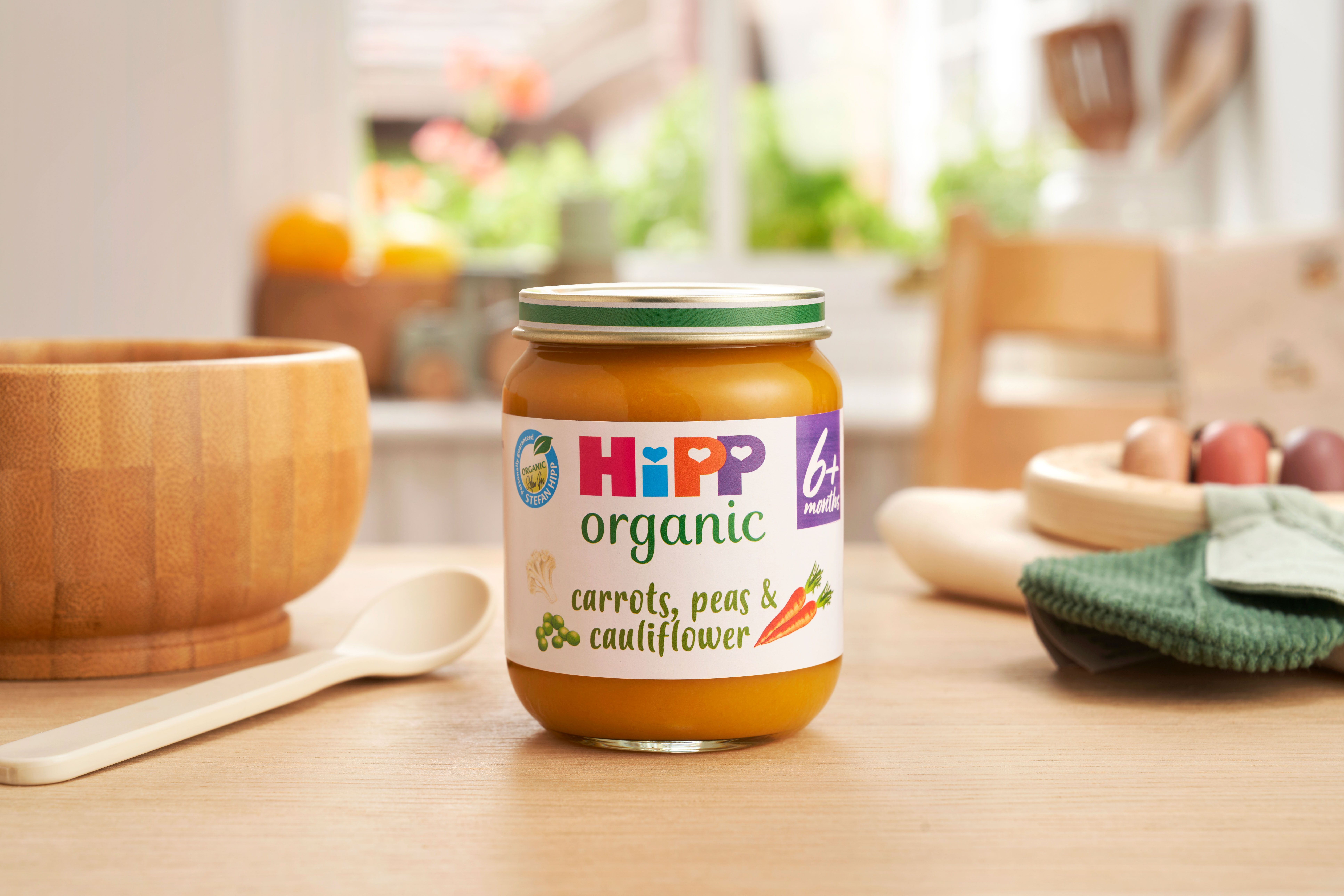 HiPP Organic Carrots, Peas & Cauliflower jar on a dining table next to a bowl and spoon