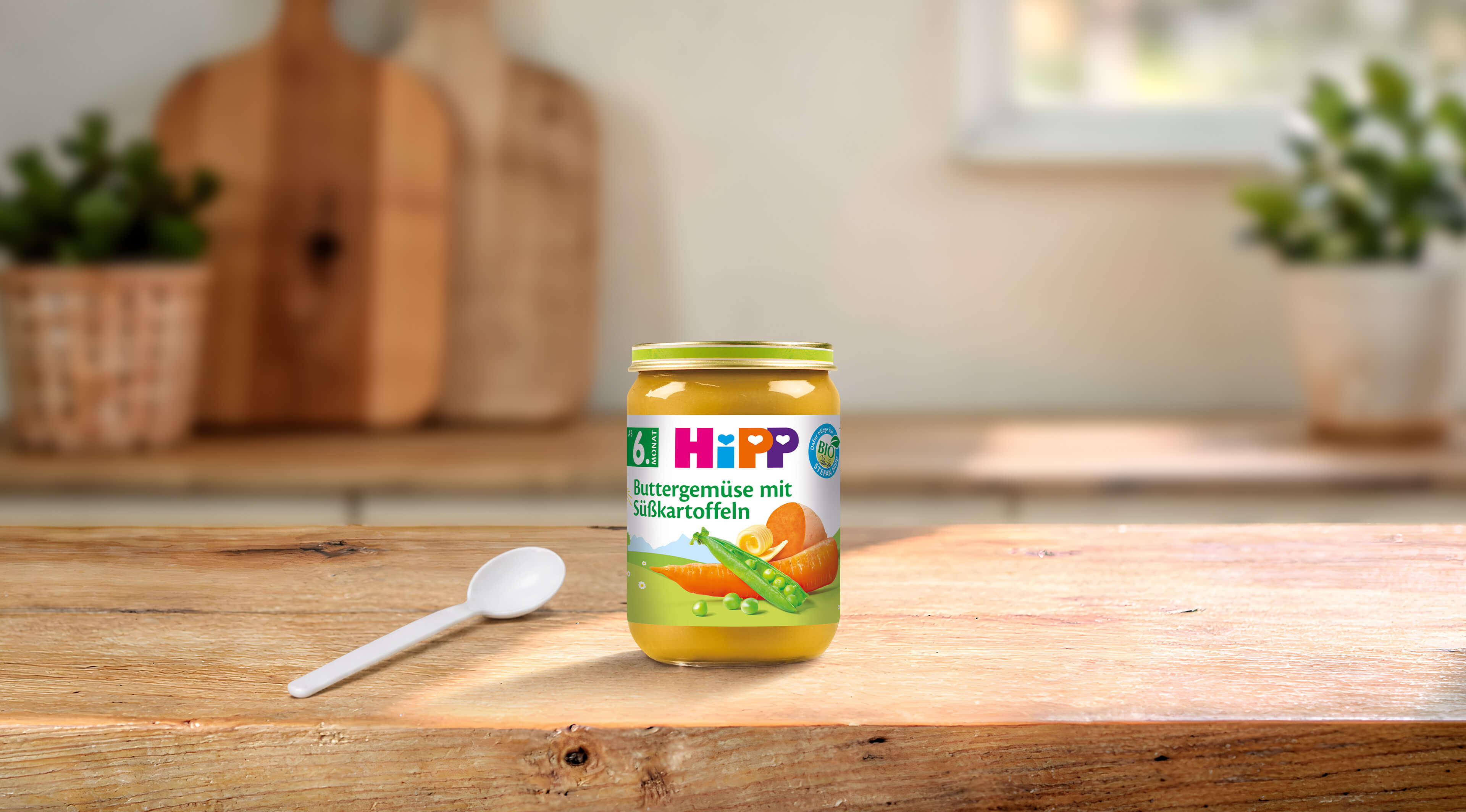 HiPP Bio-Gläschen Buttergemüse mit Süßkartoffeln ab dem 6. Monat auf Holztisch mit Löffel in heller Küche
