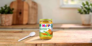 HiPP Bio-Gläschen Buttergemüse mit Süßkartoffeln ab dem 6. Monat auf Holztisch mit Löffel in heller Küche