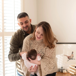 Man leading over wife's shoulder as she cradles baby.