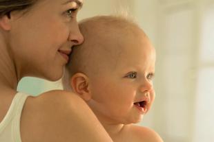 Lächelnde Mutter hält ihr fröhliches Baby dicht am Körper, Symbol für Nähe, Geborgenheit und gesunde Entwicklung