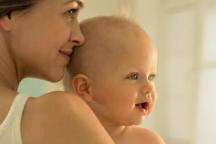 Lächelnde Mutter hält ihr fröhliches Baby dicht am Körper, Symbol für Nähe, Geborgenheit und gesunde Entwicklung
