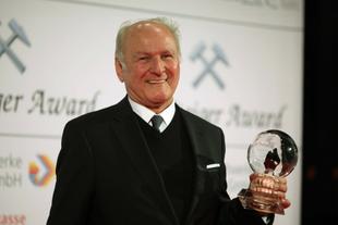 Älterer Mann im dunklen Anzug lächelt bei der Steiger-Award-Verleihung und hält eine gläserne Umwelt-Trophäe in der Hand.
