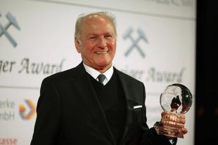 Älterer Mann im dunklen Anzug lächelt bei der Steiger-Award-Verleihung und hält eine gläserne Umwelt-Trophäe in der Hand.