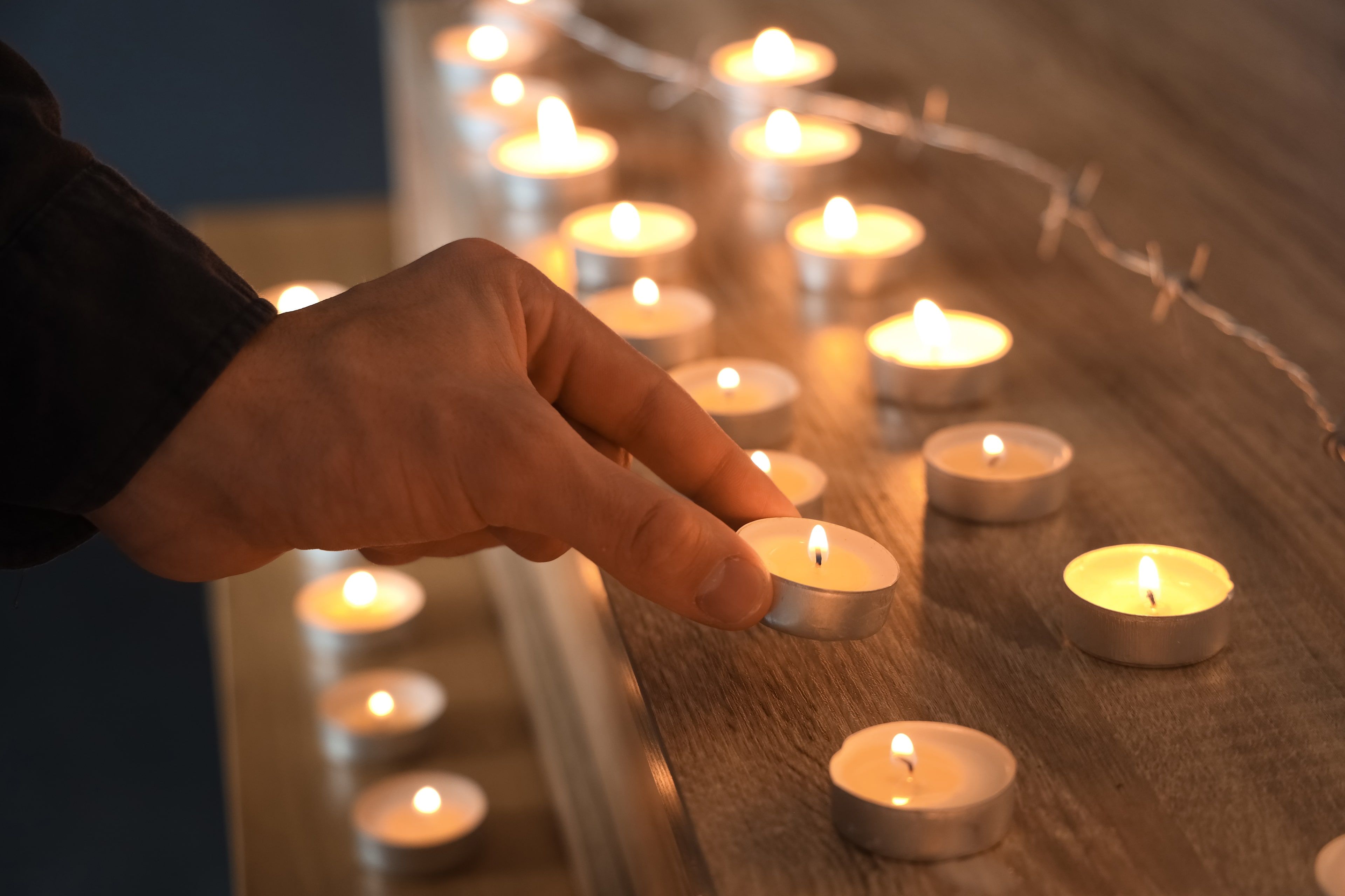 Eine Hand, die eine brennende Teelichtkerze auf eine hölzerne Oberfläche stellt, umgeben von anderen Kerzen.