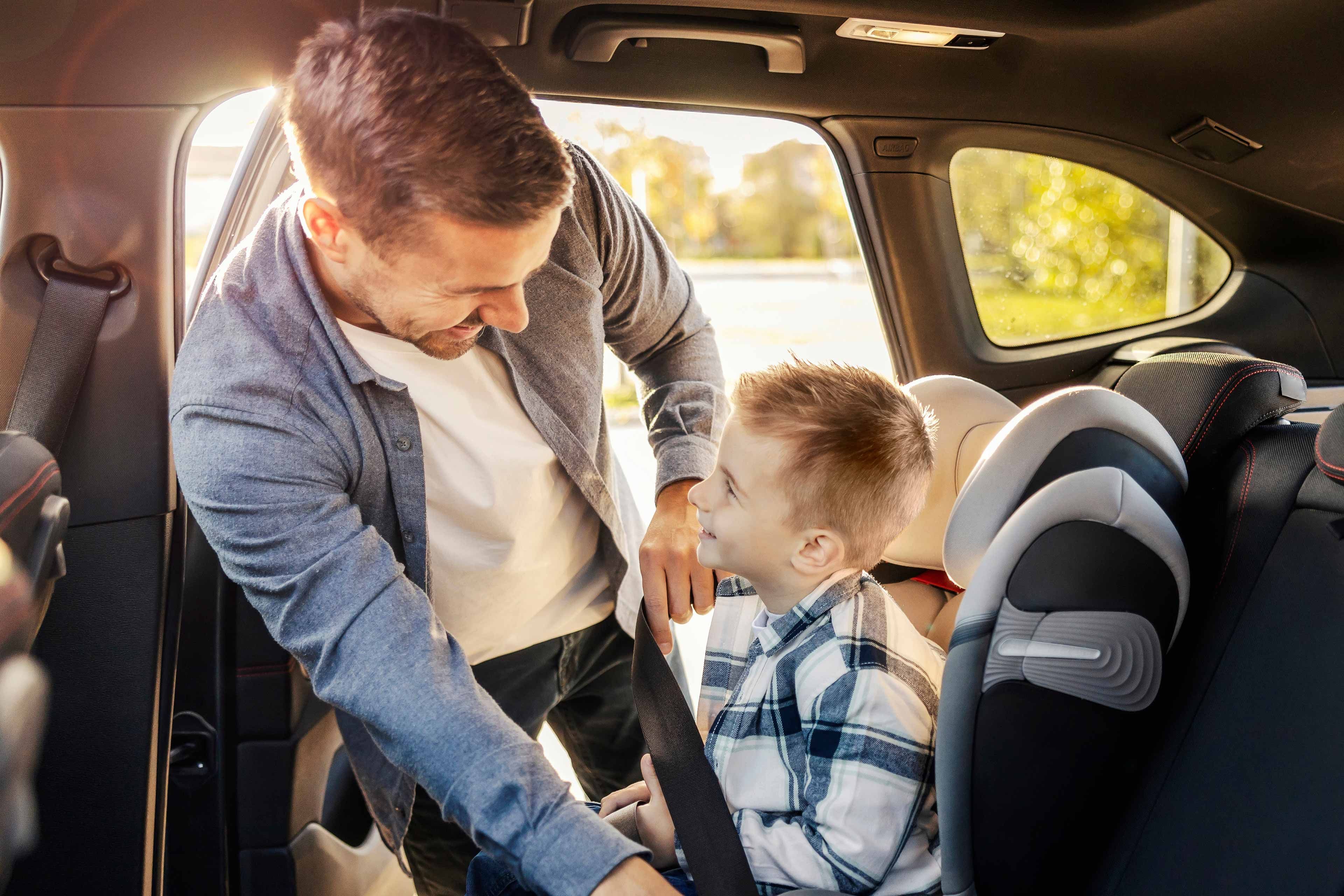 Ein Mann und ein kleiner Junge sitzen in einem Auto, wobei der Mann dem Jungen hilft, sich anzuschnallen.