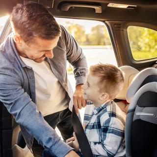 Ein Mann und ein kleiner Junge sitzen in einem Auto, wobei der Mann dem Jungen hilft, sich anzuschnallen.