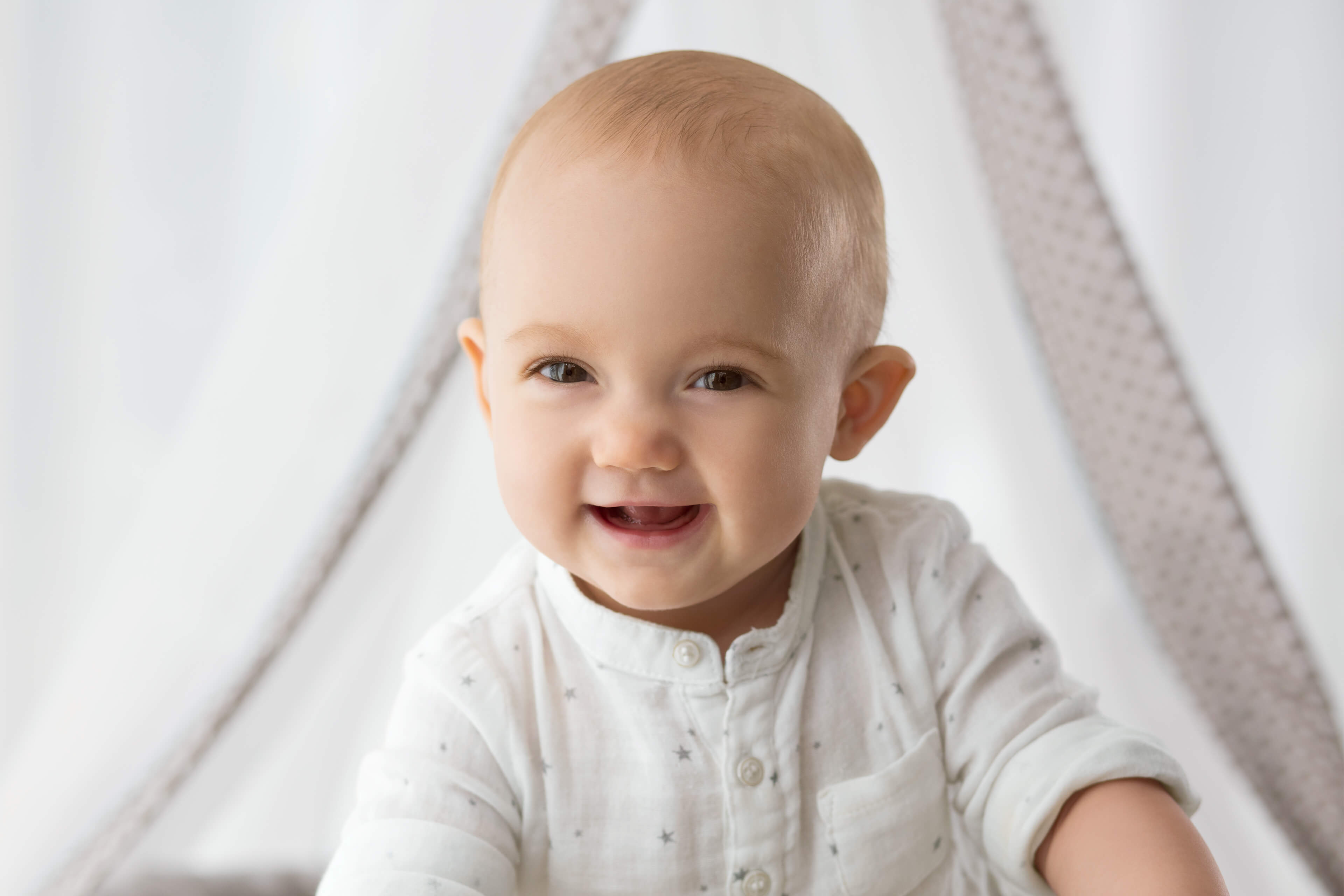 Ein Baby mit einem freudigen Gesichtsausdruck, das ein weißes Hemd trägt, vor einem weichen Hintergrund.