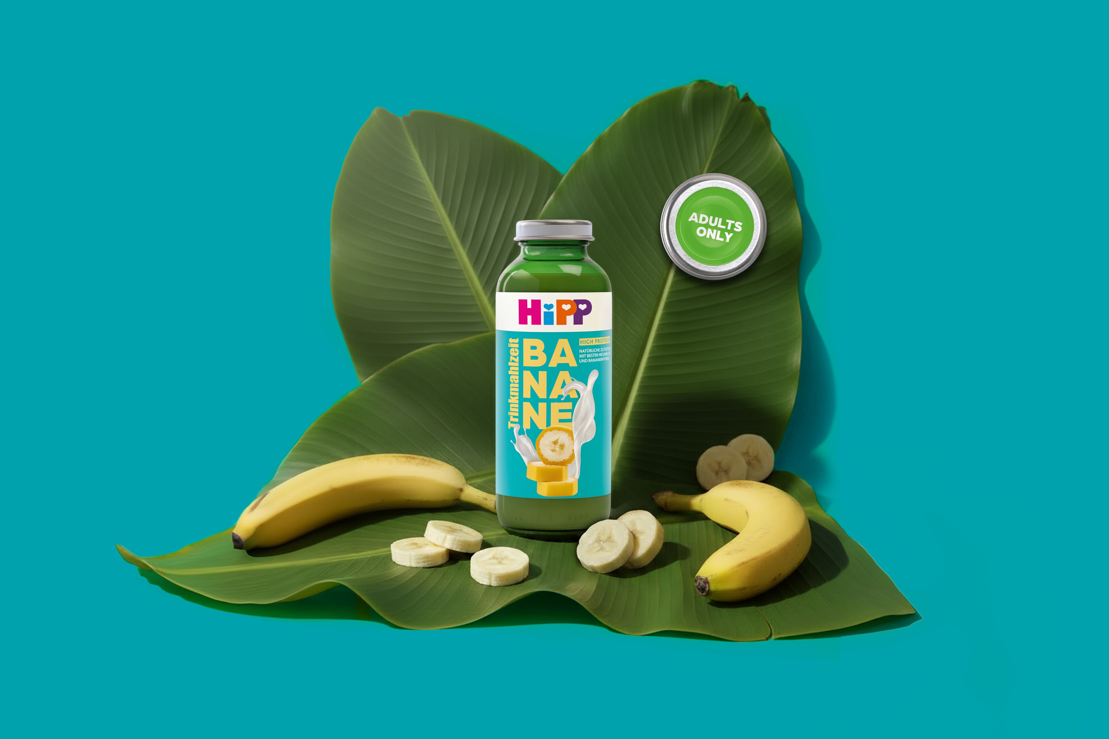 Flasche Hipp Trinkmahlzeit Banane mit Deckel und Bananenstücken auf großen grünen Blättern vor türkisfarbenem Hintergrund