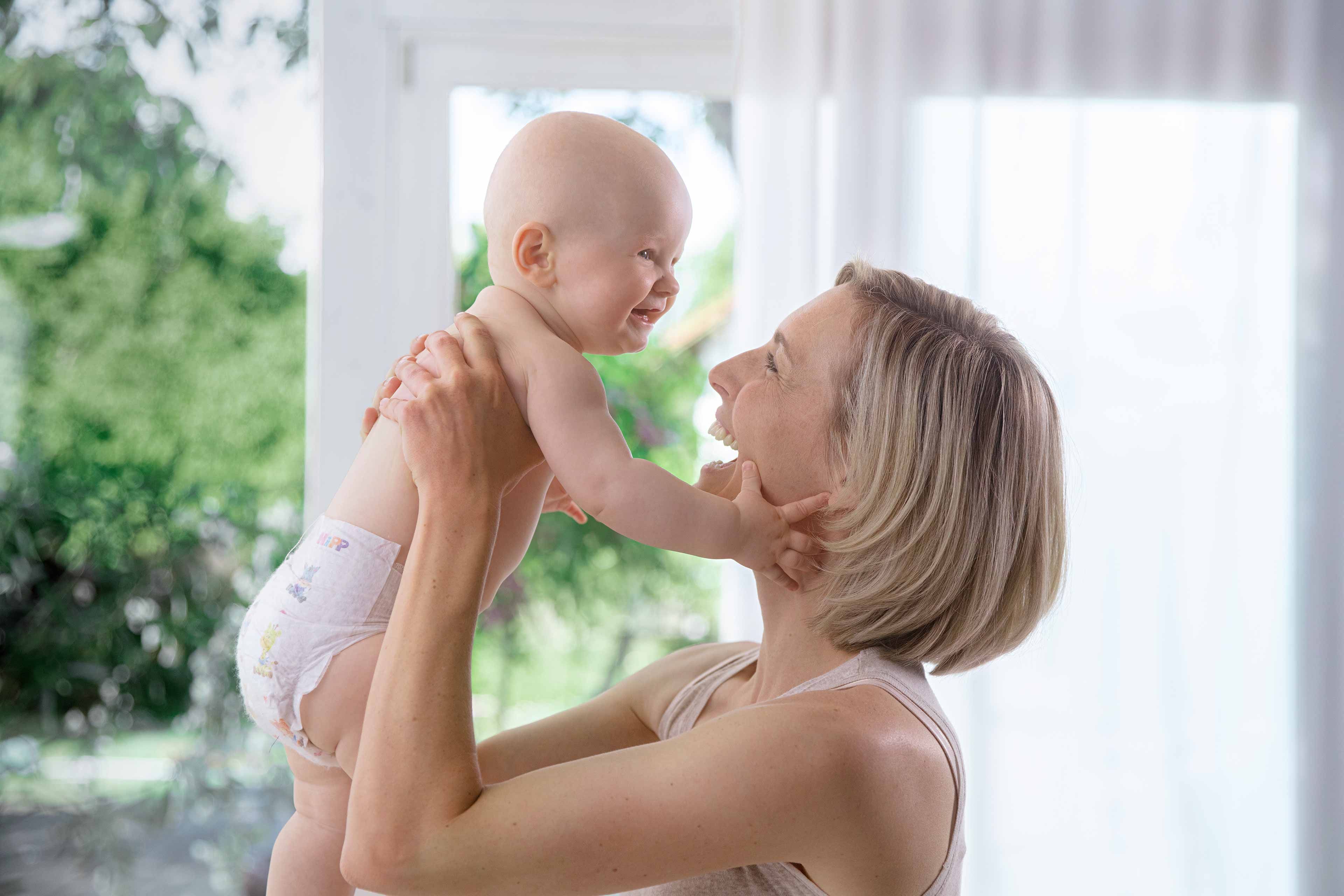 Ein zärtlicher Moment zwischen einer Mutter und ihrem Baby, in dem die Mutter das Baby freudig hochhebt und beide einen innigen Moment der Verbundenheit erleben.