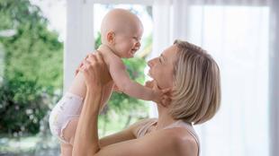 Ein zärtlicher Moment zwischen einer Mutter und ihrem Baby, in dem die Mutter das Baby freudig hochhebt und beide einen innigen Moment der Verbundenheit erleben.