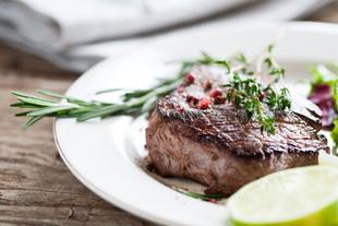Ein gegrilltes Steak, garniert mit Kräutern und Gewürzen, begleitet von einer Salatbeilage und Limettenspalten.