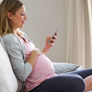 Schwangere Frau sitzt entspannt auf dem Sofa und nutzt auf ihrem Smartphone den HiPP Rechner.