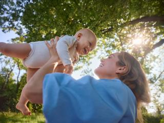 Mutter hebt ihr lachendes Baby im sonnigen Grünen hoch