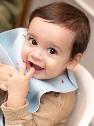 Baby boy sat in highchair playing with bib