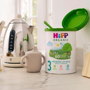 HiPP Organic Growing Up Milk Powder tin on a bright kitchen counter beside a toddler beaker and kettle, ready for milk preparation
