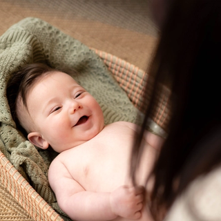 Smiling baby lying in a basket, wrapped in a green blanket.
