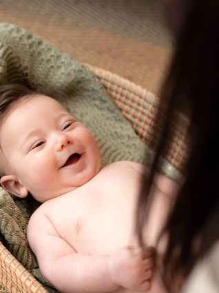 Smiling baby lying in a basket, wrapped in a green blanket.