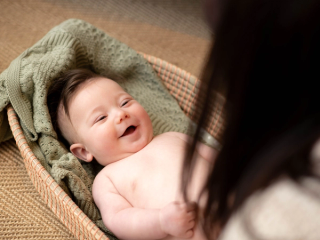 Smiling baby lying in a basket, wrapped in a green blanket.