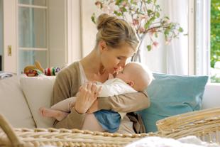 Ein zärtlicher Moment zwischen einer Mutter und ihrem Baby, in dem die Mutter sanft die Stirn des Babys küsst.