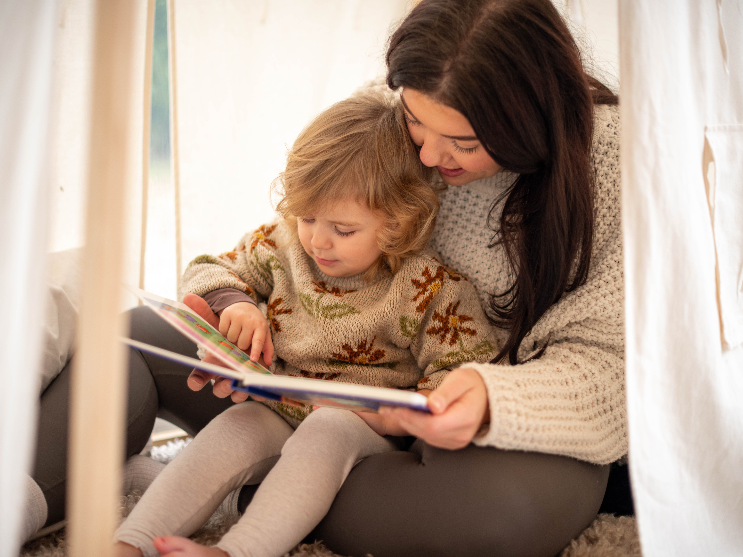 Mum reading to toddler in a play tent