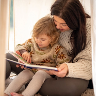 Mum reading to toddler in a play tent
